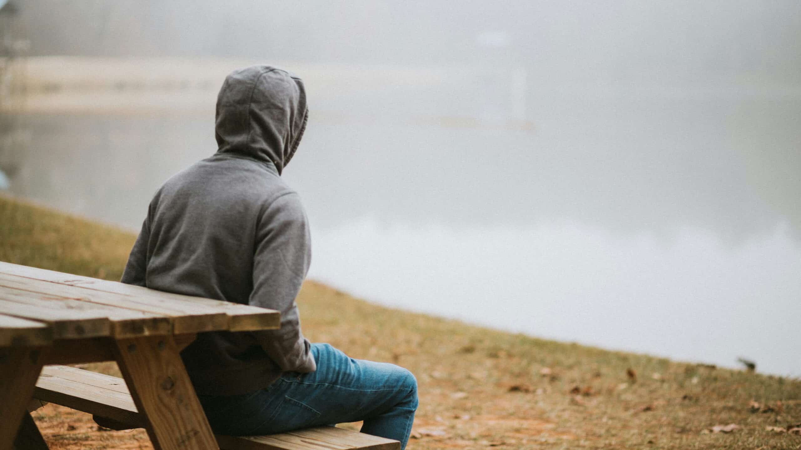 A solitary person sits looking out onto a lake