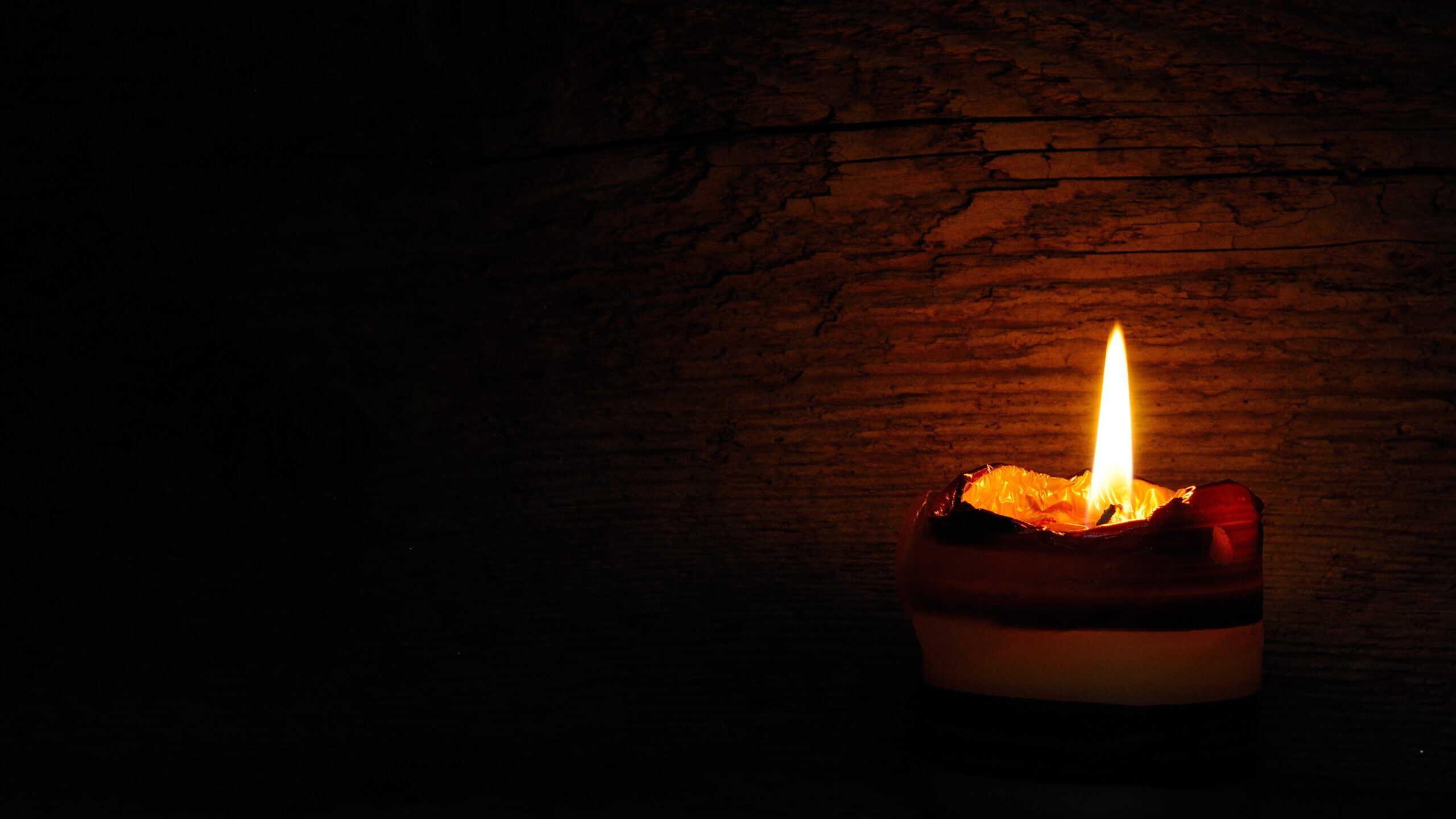 a single candle casts a dim glow on a wooden wall