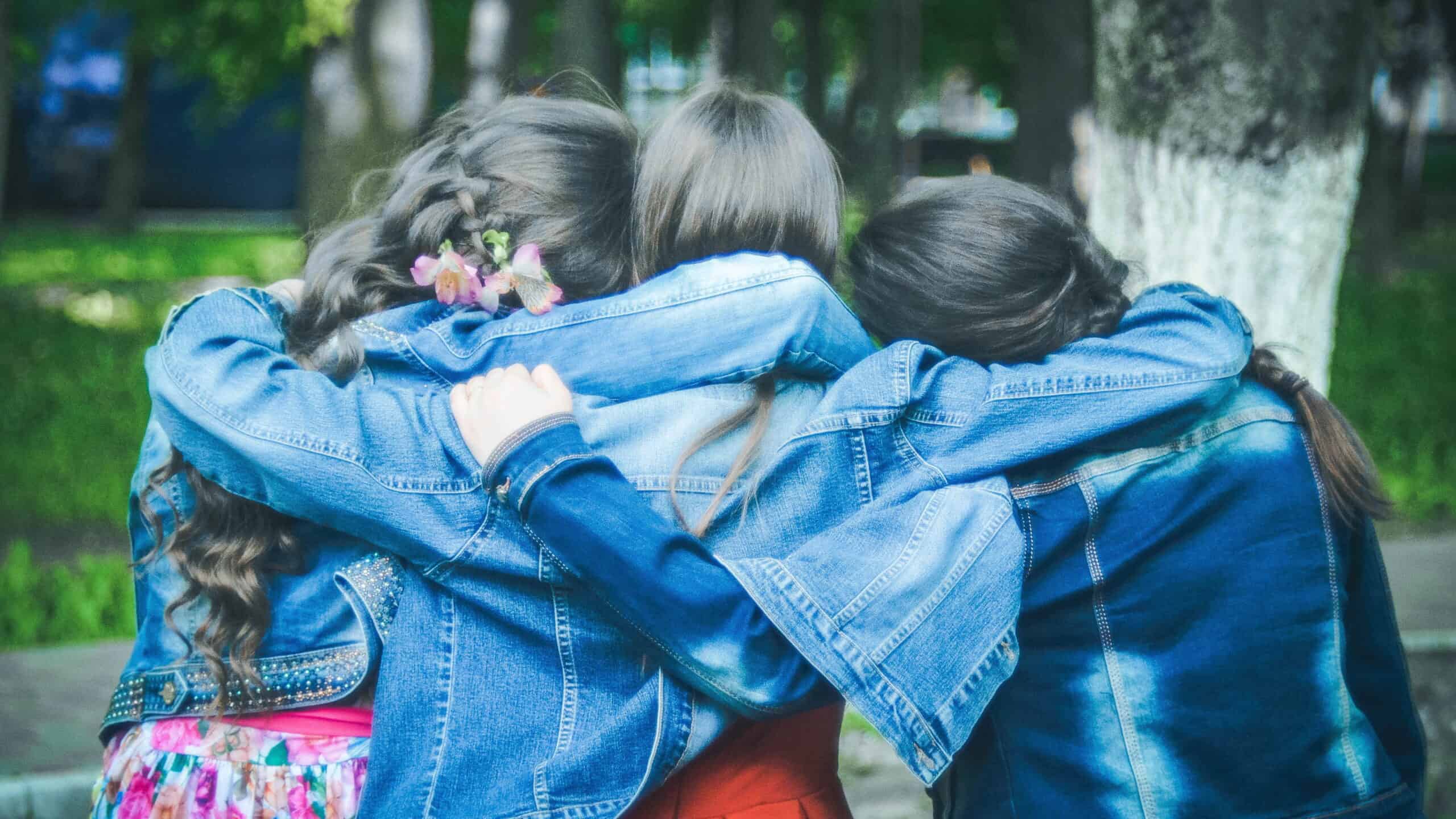 Three friends share a group hug, seen from behind.